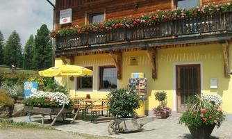 A cozy café with a yellow façade and blooming flowers. Outside, there are tables and chairs under a sunny umbrella.