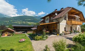 A beautiful, traditional house in the Alps with a spacious garden. The mountains and the blue sky in the background create a picturesque atmosphere.