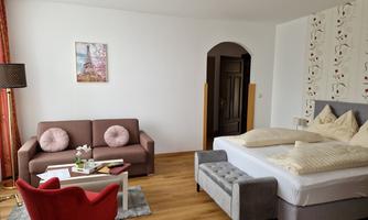 A bright room with a large bed and a cozy sofa. The decor is modern and inviting, with a beautifully decorated picture on the wall.