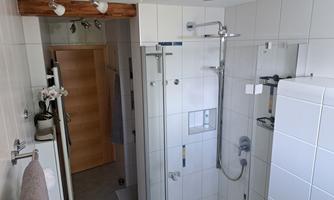 A modern bathroom with a glass shower and bright tiled floor. There are wooden details and a door to another room.