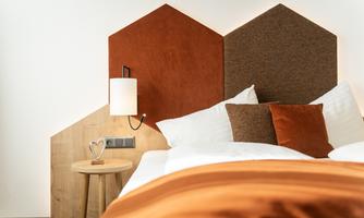 A modern bedroom with a stylish hexagon-shaped headboard. The color tones are warm and inviting, complemented by cozy bedding.