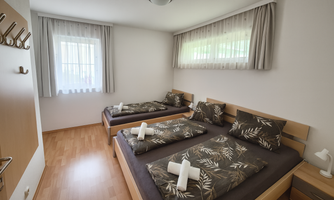 A cozy bedroom with two single beds and modern decor. The windows let in plenty of light and provide a friendly view of nature.