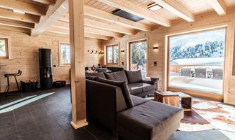 A modern living room made of wood with large windows and a view of the mountains. The decor is cozy and inviting, with a simple sofa and a table.