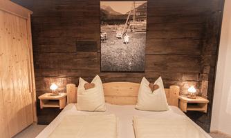 A cozy room with a large double bed and wooden furniture. On the walls, there are wooden paneling and a decorative picture.