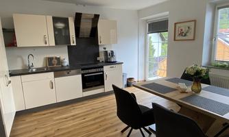 A modern kitchen with white cabinets and a wooden floor. A dining table with chairs and a vase with flowers is also present.