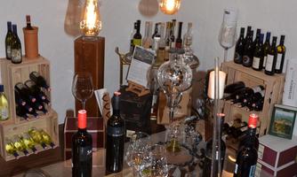 A stylishly furnished wine cellar with various wine bottles and glasses. Warm light sources hang above the table, creating a cozy atmosphere.