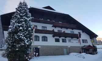 A snow-covered building with balconies and a large tree in the foreground. The surroundings depict a winter landscape.