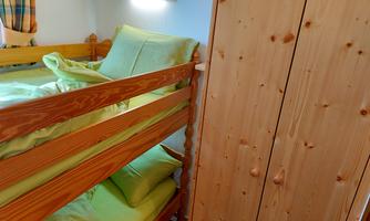 A small room with bunk beds in light wood. The bedding is in soft green tones, and in the background, there is a cupboard.