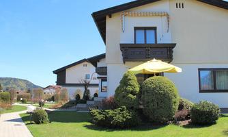 A beautiful house with a garden and a short path. The midday sun shines on a yellow sun umbrella.