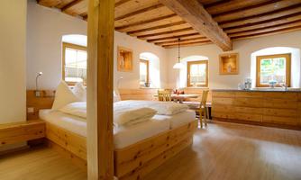 A cozy room with wooden decor and a large bed. There is a dining area and windows that let in plenty of light.