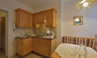 A cozy kitchen unit made of wood with modern appliances. Next to it is a seating area with a padded sofa.