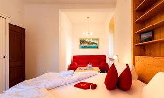 A cozy room with a double bed and a red sofa. There are wooden shelves and a colorful picture on the wall.