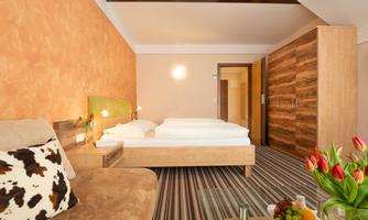 A bright and modern room with a double bed and a cozy seating area. Fresh fruit and a bouquet of flowers are on the table.