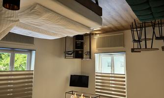A modern large room with a double bed, a cozy seating area, and a couch. Large windows let in plenty of light and give the room a pleasant atmosphere.