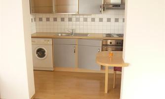 A modern kitchen with a wooden floor and light cabinets. There is a washing machine, a stove, and a small dining table.