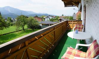 A cozy balcony with a view of green meadows and mountains. There are two chairs and a table on the balcony.