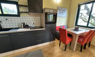 A modern kitchen with gray cabinets and a dining area. The table is surrounded by red chairs and there are large windows with a view outside.