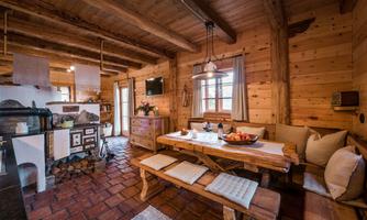 A cozy wooden cabin with a large dining table and a modern kitchen. The walls are made of wood, creating a warm atmosphere.