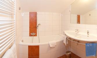 A clean bathroom with a bathtub, two sinks, and modern design. The walls are light tiled, and the floor has brown tiles.