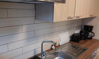 A modern kitchen with wooden surfaces and a cooktop. In the background, kitchen appliances and a sink are visible.