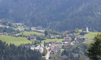 A picturesque village in the mountains with green meadows and scattered houses. In the center stands a church, surrounded by a beautiful landscape.