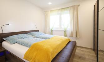 A modern bedroom with a large double bed and bright curtains. The walls are kept neutral, and the room has a warm, inviting look.