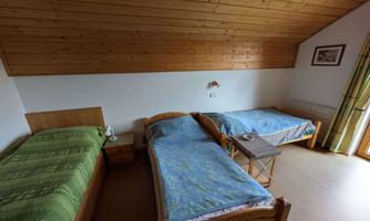 A simple bedroom with two single beds and wooden walls. A table with a lamp stands between the beds and the window is brightly lit.