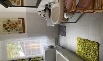 A modern bathroom with a bathtub, a sink, and a washing machine. The room is bright and friendly, with colorful pictures and a green carpet.