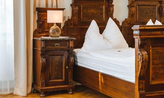 A bedroom with an elegant wooden bed and white pillows. Next to the bed stands a nightstand with a lamp.