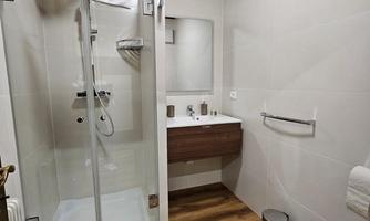 A modern bathroom with a shower and a washbasin. The floor is made of wood, and the walls are brightly tiled.