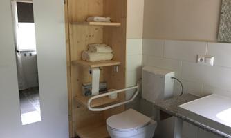 A modern bathroom with a toilet, a sink, and wooden shelves. Fresh towels are placed on the shelves.