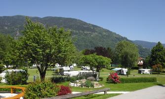 A beautiful campsite with RVs and green meadows. In the background, there are mountains and a clear blue sky.