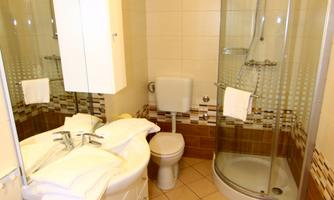 A modern bathroom with a shower, sink, and toilet. The walls are lightly tiled and the floor has a slight texture.