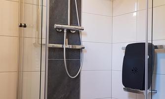 A modern shower with a glass partition and a stylish tiled floor. The fittings and the handheld shower are made of stainless steel and look elegant.