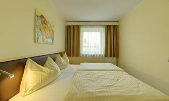 A simple room with two single beds and a large window. The walls are in soft colors, and there are curtains with a striped pattern.
