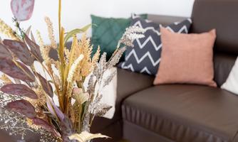 A stylish living room with a brown sofa and decorative cushions. A bouquet of dried flowers adorns the table.