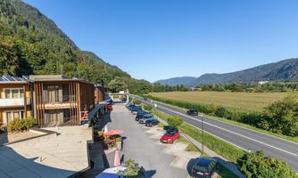 A picturesque landscape with a hotel located on a quiet road. In the background, mountains and a green meadow can be seen.