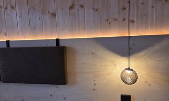 A cozy room with wood paneling and soft lighting. A hanging lamp provides warm light over a bench.