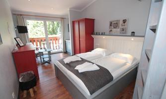 A cozy bedroom with two beds and modern furniture. Large windows offer a view outside and plenty of daylight.