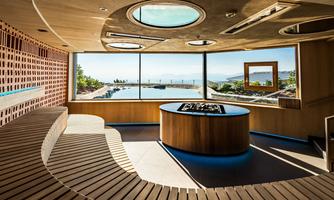 A stylish interior with wooden paneling and large windows that offer a view of a pool and the landscape. The round bar in the center gives the room a cozy atmosphere.