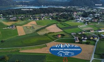 An aerial shot of a picturesque landscape featuring fields, a lake, and mountains in the background. The logo of Bungalows Bergpanorama is in focus.