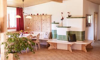 A bright and inviting living space with a cozy dining area and traditional wooden interior. The green tiled bench and red curtains give the room a warm atmosphere.
