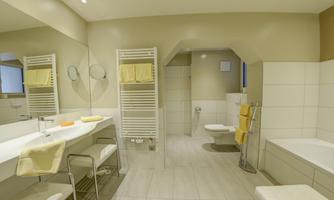 A modern bathroom with bright tiles and a large mirror. There are bright towels and a bathtub.