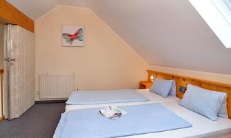 A cozy room in the attic with two single beds and blue bedding. A small window provides daylight and a relaxed atmosphere.