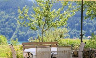 A cozy outdoor seating area with a table and chairs under a sun umbrella. In the background, green trees and gentle hills can be seen.