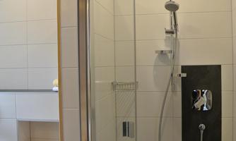 A modern bathroom with a glass shower and elegant fixtures. The walls are brightly tiled and the ambiance is clean and minimalist.