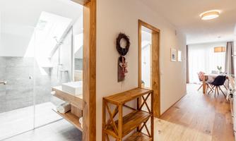 A modern hallway with wooden details and bright light. On the left side, a bathroom with a glass shower is visible.