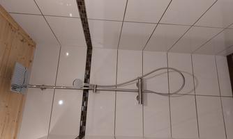A modern shower with matte white tiles and a wooden ceiling. The shower fixture is made of stainless steel and offers a simple elegance.