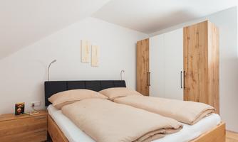 An elegant bedroom with a large double bed and beige bedspreads. In the background, there is a bright wooden wardrobe.