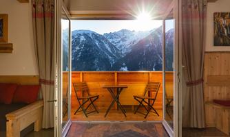A cozy holiday apartment with a view of snow-capped mountains. The balcony door is open, letting the sun in.